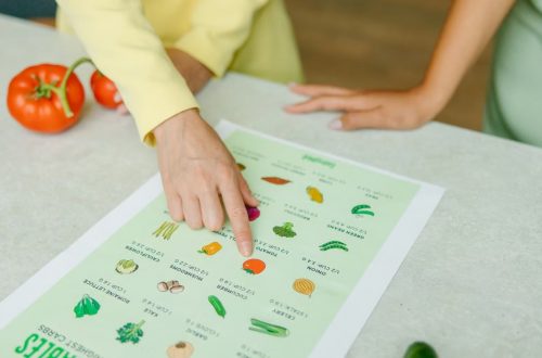 Close-up of hands pointing to a vegetable nutrition chart with fresh tomatoes on the table.