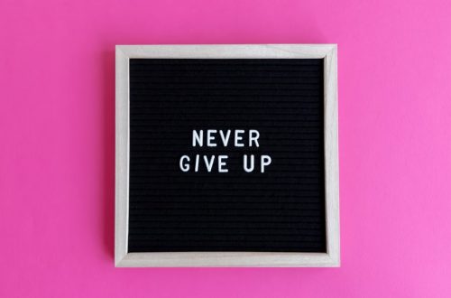 A framed letter board with 'NEVER GIVE UP' on a vibrant pink background.