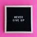 A framed letter board with 'NEVER GIVE UP' on a vibrant pink background.